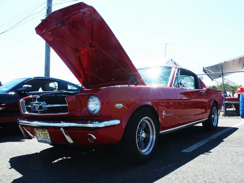 Red 1965 Ford Mustang coupe with hood open, showing chrome grille and 'K CODE' license plate