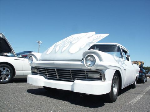2001 Mercury Grand Marquis - A white 1957 Ford Fairlane hot rod with flame decals is displayed at a car show with its hood open.