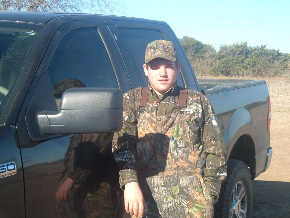 Person in camo standing beside a dark Ford pickup with 5.4 Triton badge in a rural setting