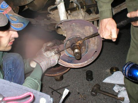 1978 Ford Bronco - Close-up of a mechanic performing maintenance on a vehicle's brake rotor and hub assembly, with tools scattered on the ground.