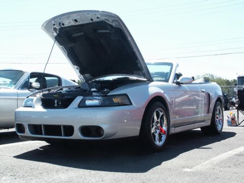 2001 Mercury Grand Marquis - A silver convertible Mustang is parked with its hood open, revealing the engine bay. Another car is visible to the left.
