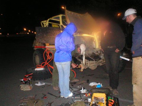 1978 Ford Bronco - Nighttime scene of mechanics working on a vehicle's suspension system with tools and equipment laid out.