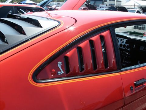 2001 Mercury Grand Marquis - A red car with distinctive louvers and a cobra emblem is seen at a car show.
