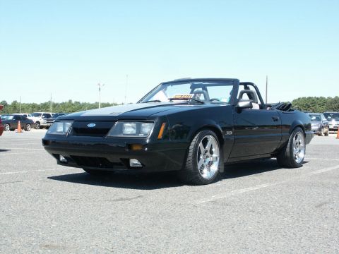 2001 Mercury Grand Marquis - A black convertible Ford Mustang is parked in a lot with other vehicles visible in the background.