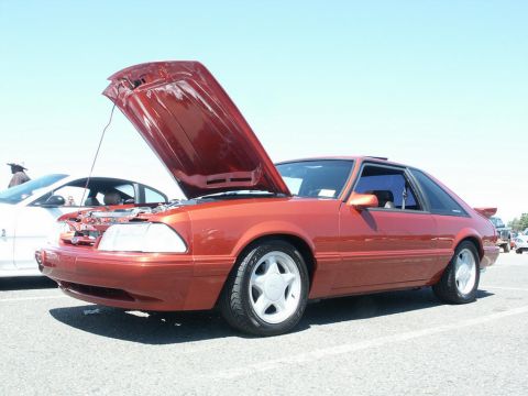 2001 Mercury Grand Marquis - Orange Ford Mustang coupe with hood open at a car show.