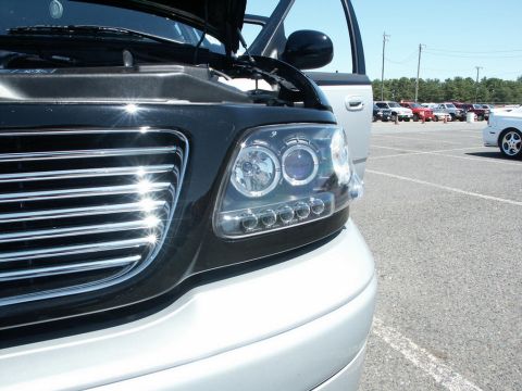 2001 Mercury Grand Marquis - Close-up of a truck's front end with aftermarket headlights and a chrome grille, parked in a lot with other vehicles.