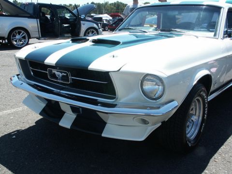 2001 Mercury Grand Marquis - A classic white 1967 Ford Mustang with teal racing stripes is displayed at a car show, with other vehicles in the background.