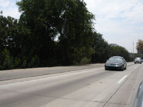 1993 Ford Taurus - A dark sedan travels down a highway with trees lining the side.
