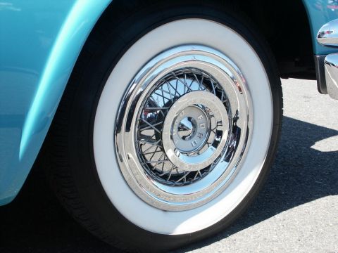 2001 Mercury Grand Marquis - A close-up shot focuses on the whitewall tire and chrome wire wheel of a classic blue automobile, a Ford emblem on the hubcap.