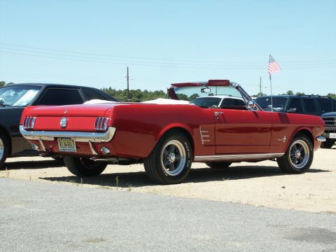 2001 Mercury Grand Marquis - A red 1965 Ford Mustang convertible is parked at a car show, seen from the rear with an American flag in the background.