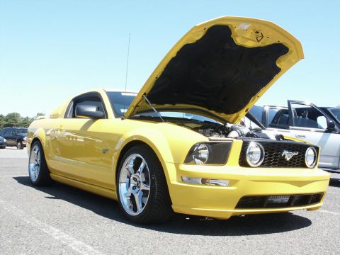 2001 Mercury Grand Marquis - A yellow 2005 Ford Mustang GT is displayed with its hood open at a car show.