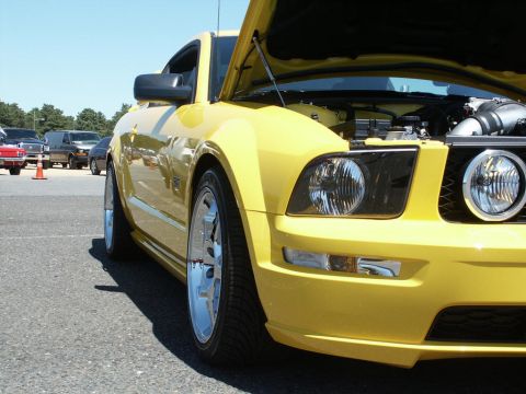 2001 Mercury Grand Marquis - A yellow Ford Mustang is parked at a car show with its hood up, revealing the engine bay.