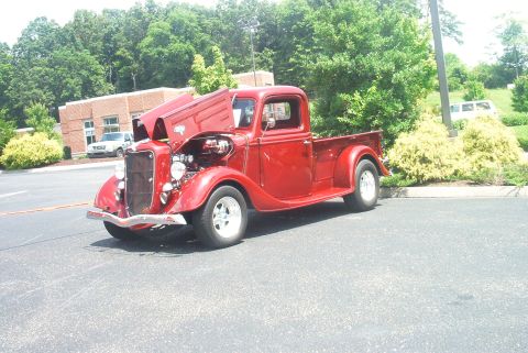 1985 Ford Crown Victoria LTD - A classic red pickup truck is parked in a lot with its hood open, revealing the engine.