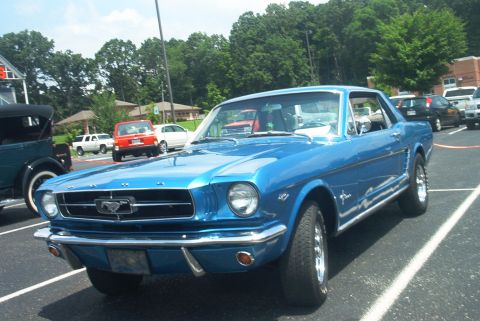 1985 Ford Crown Victoria LTD - A bright blue 1965 Ford Mustang coupe is parked in a lot with other vehicles visible in the background.