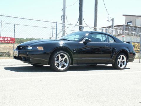 2001 Mercury Grand Marquis - A black Ford Mustang is parked outdoors near a fence and a building.