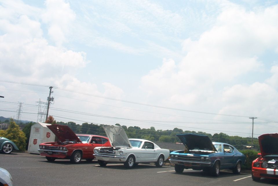 Several classic cars parked outdoors with hoods open