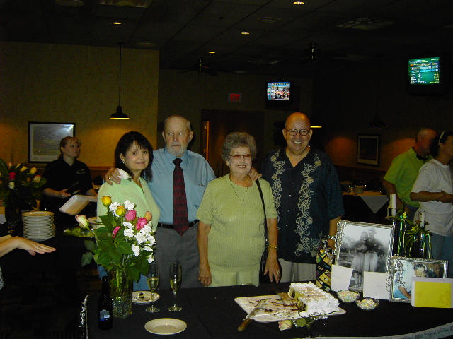 People gathered around a table with a cake and framed photos at a celebration