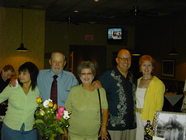 Five people posing for a photo indoors, with a bouquet of flowers in the foreground
