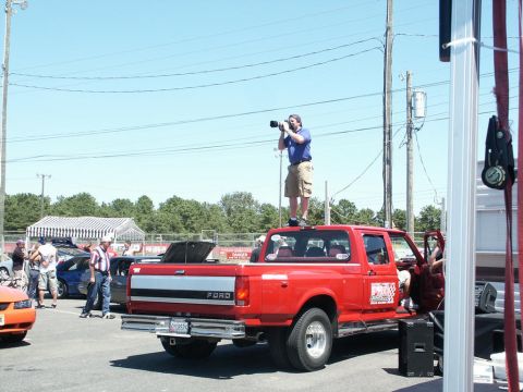 2001 Mercury Grand Marquis - A photographer stands on the roof of a red Ford pickup truck at an outdoor event.