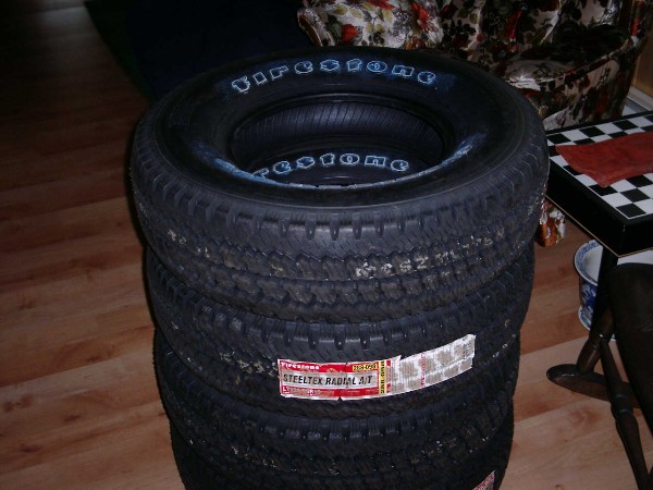 Stack of four new Firestone Steeltex Radial A/T all-terrain tires with retail labels indoors