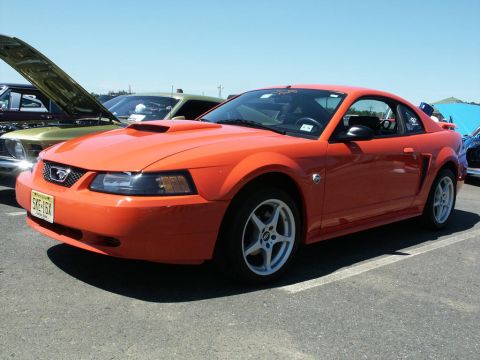 2001 Mercury Grand Marquis - An orange Ford Mustang is parked at a car show, with other vehicles visible in the background.