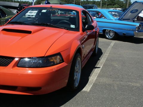 2001 Mercury Grand Marquis - An orange Ford Mustang is parked at a car show next to a blue classic car with its hood open.