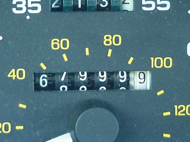 Close-up of a mechanical odometer reading near 67,999 with yellow speedometer arcs