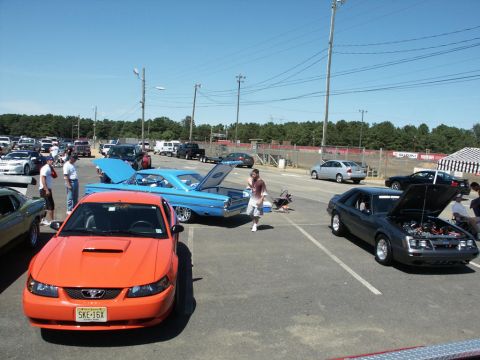 2001 Mercury Grand Marquis - An orange Ford Mustang is parked at a car show with its hood scoop visible and a license plate reading SKE-16X.