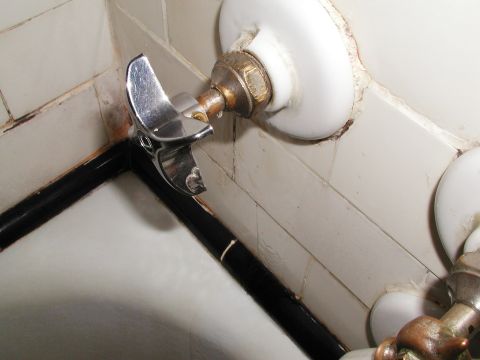 1992 Ford Taurus - A close-up view of a chrome faucet attached to a pipe against a tiled wall.