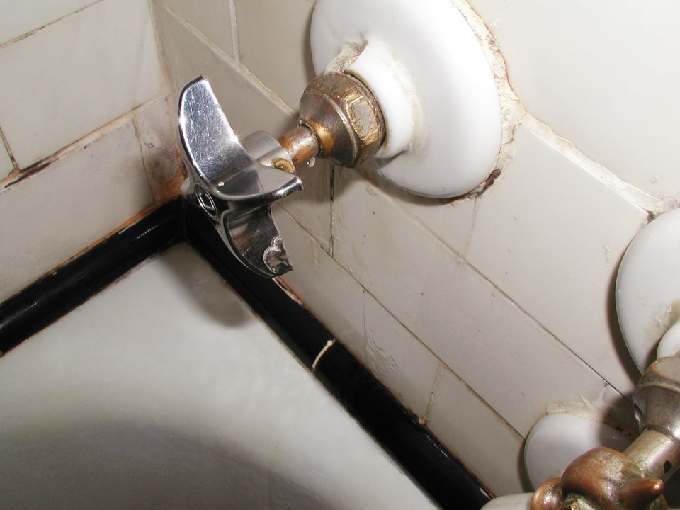 Chrome faucet with a black pipe and white tiled wall