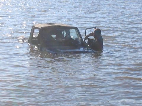 1990 Ford Bronco - A person exits a Jeep Wrangler that is partially submerged in water.