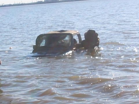 1990 Ford Bronco - A vehicle is partially submerged in the water with people inside.