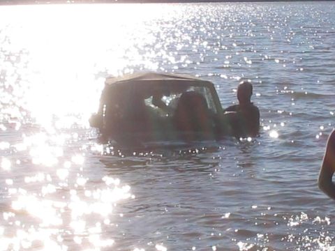 1990 Ford Bronco - An SUV is partially submerged in water, with several people in and around the vehicle.