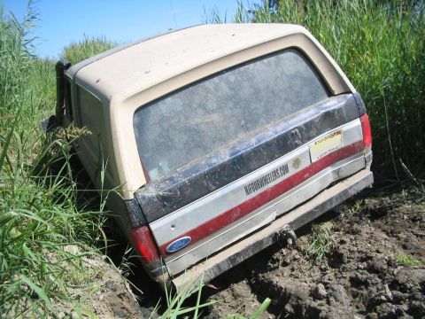 1990 Ford Bronco - This 1990 Ford Bronco is stuck deep in the mud, with tall grass surrounding it.
