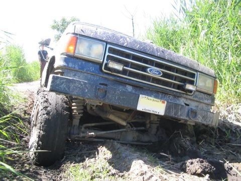 1990 Ford Bronco - A Ford truck navigates a muddy trail, with its front tires deep in the muck.