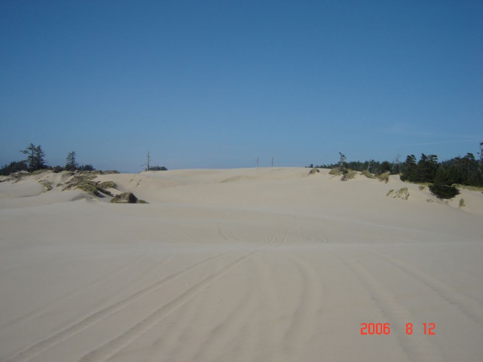 Sand dunes with tire tracks under a clear blue sky. A watermark reads 'SUPERMOTORS.NET'