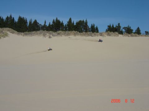 1993 Ford Bronco - ATVs kicking up dust while riding on a sandy dune landscape under a clear blue sky.