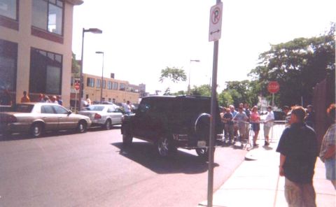 1993 Ford Taurus - A black SUV with a spare tire mounted on the rear is parked on a street, observed by a crowd of onlookers.