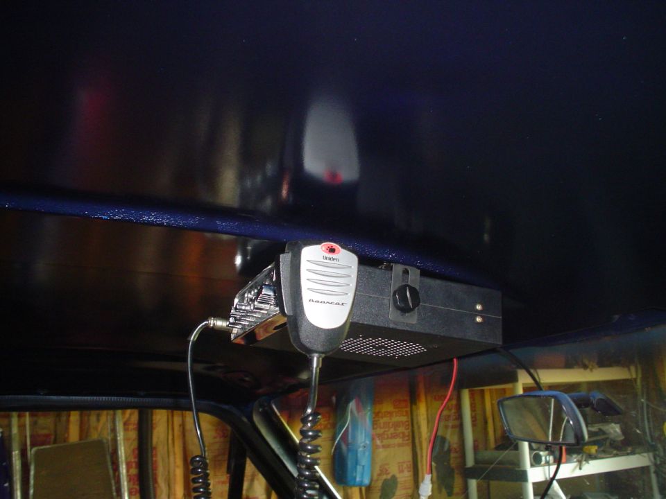 CB radio and microphone attached to the ceiling of a vehicle, with a side mirror visible