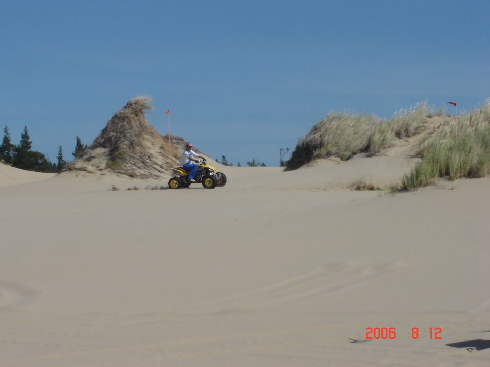Yellow ATV with rider on a sand dune under a blue sky