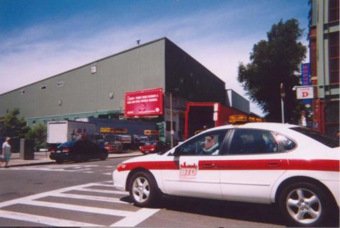 1993 Ford Taurus - A 1993 Ford Taurus taxi drives down the street past a large building.