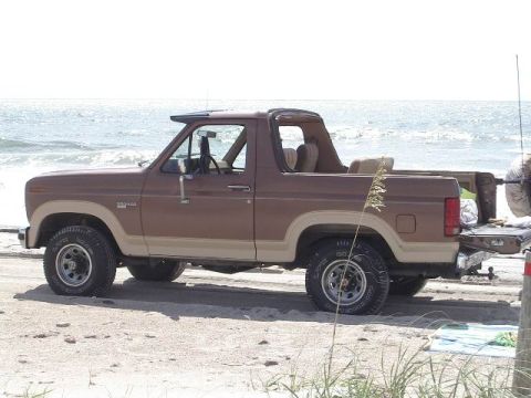 1985 Ford Bronco - This 1985 Ford Bronco is parked on the beach with the ocean waves visible behind it.