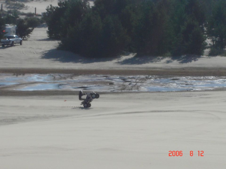 ATV on its side in sand with a pickup truck and trailer in background