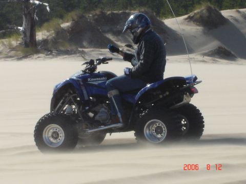 1993 Ford Bronco - A person rides a blue Kawasaki ATV through sandy terrain, kicking up dust.