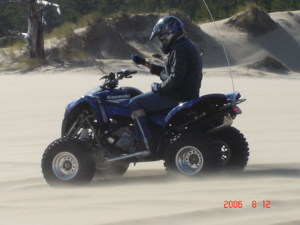 Rider on a blue Kawasaki ATV kicking up sand on a dune
