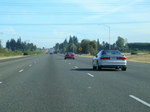 1996 Ford Probe - A silver 1996 Ford Probe convertible drives down the highway, seen from behind. Another red car is ahead on the road ahead.