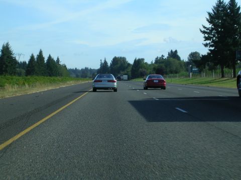 1996 Ford Probe - Two cars are driving on a highway on a sunny day with trees lining the road.