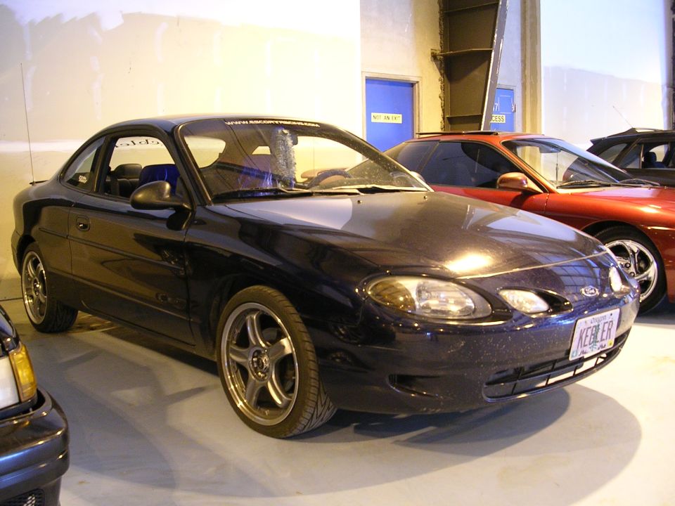 Dark 1996 Ford Probe coupe with aftermarket wheels, parked next to a red car