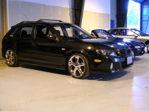 1996 Ford Probe - A black hatchback with custom chrome wheels is parked next to other vehicles in an indoor space.