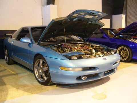 1996 Ford Probe - A light blue Ford Probe is parked with its hood open, revealing the engine bay. Another vehicle is visible to the right.